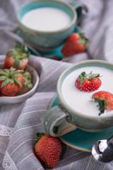 Fresh strawberries and cup of milk on a tablecloth.