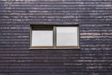 Single window in the wall covered with wooden weathered brown planks. Construction materials of building exterior.