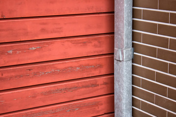 Materials of building exterior. Texture of wooden red wall planks with brown bricks and metal water pipe.