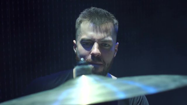 Close-up face of emotional bearded male drummer playing drums on a black background.