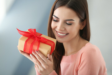 Beautiful young woman holding gift box at home