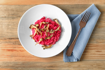 Plate of tasty beetroot risotto with mushrooms on table, top view