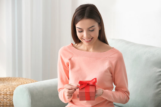 Beautiful young woman holding gift box at home
