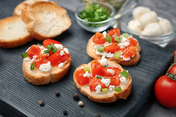 Tasty bruschettas with tomatoes on wooden board, closeup