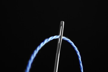 Needle with sewing thread on black background, closeup