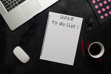 Laptop, mouse and other supplies with cup of coffee with text " 2018 to do list". Wooden black office desk table with top view angle .