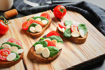 Tasty bruschettas with cherry tomatoes and mozzarella on wooden board