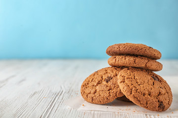 Delicious oatmeal cookies with chocolate chips on wooden table against color background
