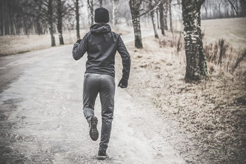 Young man running away on runway at street in the dark cloudy afternoon. Daily outdoor active lifestyle. Enjoying sport concept. Runner's back.