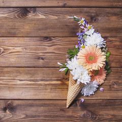 Fototapeta na wymiar Waffle cones with flowers on a wooden background