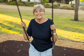 happy portrait of American senior mature beautiful woman on her 70s sitting on park swing outdoors relaxed smiling and having fun in healthy aging