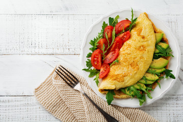 Omelette with avocado, tomatoes and arugula on white ceramic plate on light stone background. Healthy breakfast. Selective focus. Top view. Copy space.