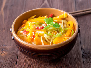 Asian cuisine, noodles stir-fry udon with vegetables. Pepper, carrot, leek, sesame and teriyaki sauce on a brown wood table, side view, close up.