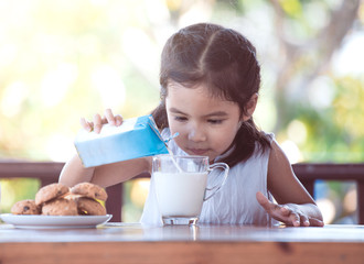 Cute asian little child girl pouring milk into glass for breakfast