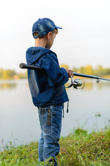 A fisherman boy on the river bank with a fishing rod in his hands. He wants to catch a big fish..