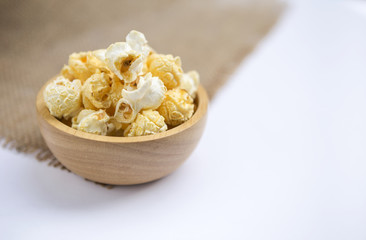 Closeup salted popcorn in round wooden bowl on white background, unhealthy snack