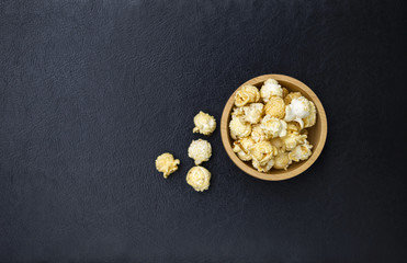 Obraz na płótnie Canvas Salted popcorn in round wooden bowl on black leather texture background, movie night snack