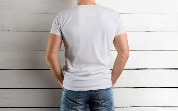 Rear view on the back of an athletic Caucasian guy in a white T-shirt on a wooden background