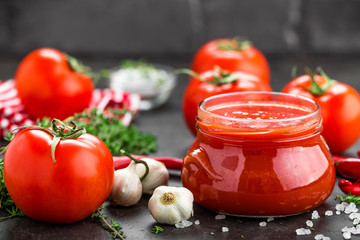 Tomato paste, puree in glass jar and fresh tomatos on dark background. Hot vegetable sauce with chili pepper and tomatoes