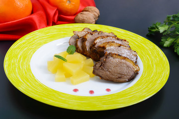 Duck breast Magret with pieces of pineapple on a ceramic plate on a black background. French traditional meat dish. Christmas menu. Festive kitchen.