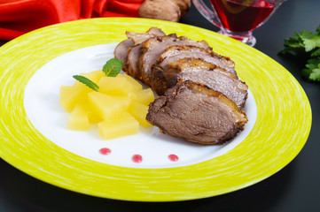 Duck breast Magret with pieces of pineapple on a ceramic plate on a black background. French traditional meat dish. Christmas menu. Festive kitchen.