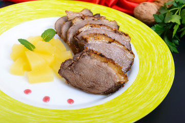 Duck breast Magret with pieces of pineapple on a ceramic plate on a black background. French traditional meat dish. Christmas menu. Festive kitchen.