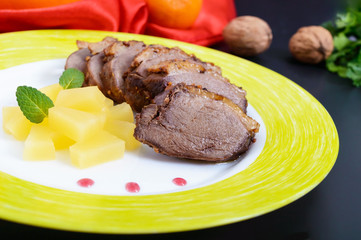 Duck breast Magret with pieces of pineapple on a ceramic plate on a black background. French traditional meat dish. Christmas menu. Festive kitchen.