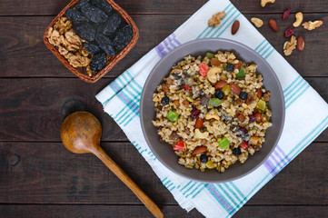 Wheat porridge with nuts, dried berries, raisins, poppies in a ceramic bowl on a dark wooden background. Proper nutrition. Healthy food. The top view