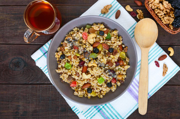 Wheat porridge with nuts, dried berries, raisins, poppies in a ceramic bowl on a dark wooden background. Proper nutrition. Healthy food. The top view