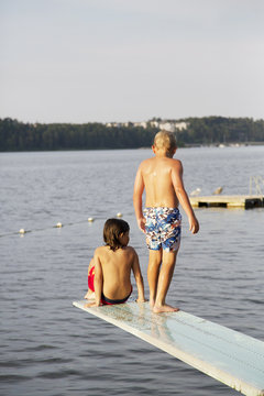 Two boys on springboard over lake