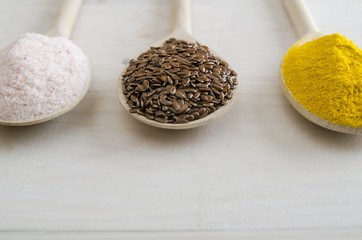 different spices in wooden spoons on a white wooden background