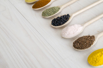 different spices in wooden spoons on a white wooden background