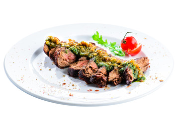 Juicy grilled beef steak with sauce pesto in a white plate, isolated on white background