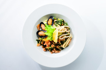 Fresh seafood salad with prepapred clams, shrimp and lemon in a white plate isolated on white background