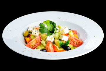 Greek salad with fresh vegetables, feta cheese and olives in a white plate isolated on black background