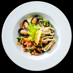 Fresh seafood salad with prepapred clams, shrimp and lemon in a white plate isolated on black background