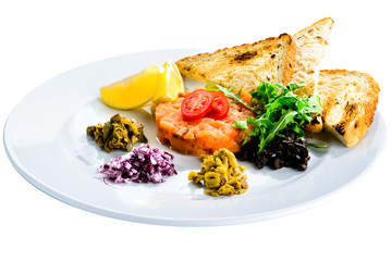 Fresh Salmon Tartare with croutons, salad and lemon slices  in a white plate isolated on black background, close-up
