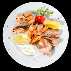 Appetizing Tuna steak with tomato, lemon and sauce in a white plate isolated on black background. Top view, flat lay