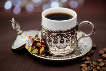 Traditional Turkish coffee in traditional metal cup on brown background with Turkish delight and bokeh