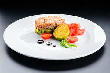 Tasty Tuna Tartare with lime, ginger and avocado in a white plate isolated on black background, close-up