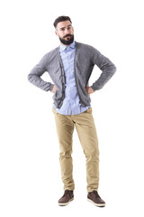 Fototapeta premium Skeptical young fashionable bearded man with arms on hips looking at camera. Full body length portrait isolated on white studio background.