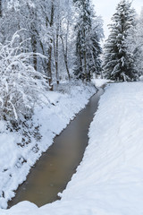 Frozen canal winter landscape with fir trees and heavy snow covering everything