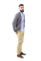 Fototapeta premium Young stylish bearded man in cardigan with hands in back pockets looking at camera. Full body length portrait isolated on white studio background. 