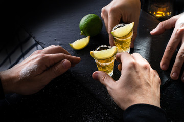 Process of drinking gold Mexican tequila with lime and salt on dark table