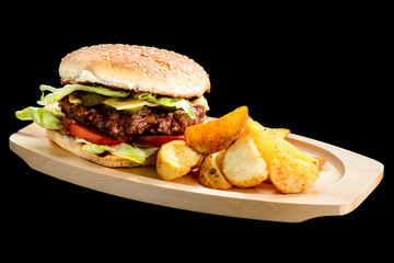 Tasty Cheeseburger with beef meat, cheese, tomato, cucumber and potato wedges on wooden board, isolated on black background