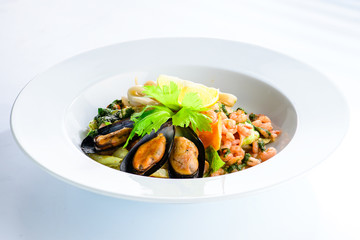 Fresh seafood salad with prepapred clams, shrimp and lemon in a white plate on gray background