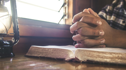 Close up hands folded of man praying on holy bible wiht oil lamp in the morning.