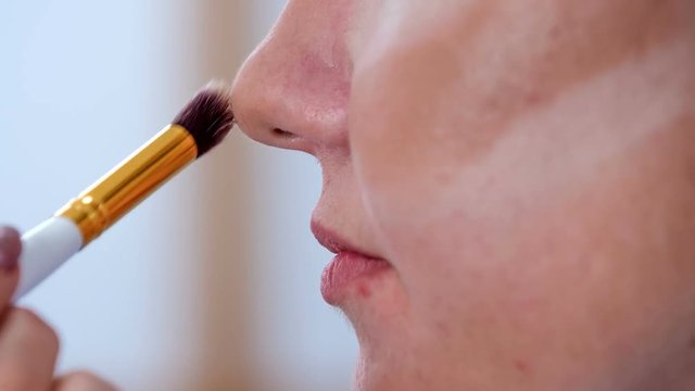 A make up artist puts a concealer on the client's nose and the area around her nose.