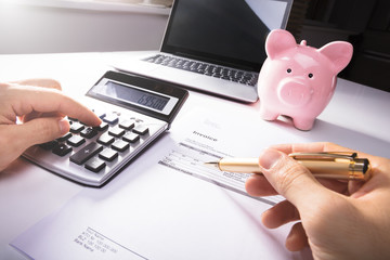 Businessperson's Hand Calculating Invoice With Calculator