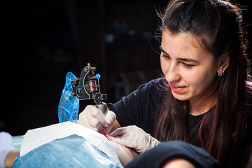 Professional tattoo artist woman makes a tattoo on a young girl's femur